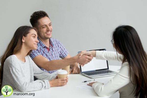 Happy millennial couple smiling, greeting advisor or consultant making good first impression. Husband handshaking real estate agent after successful contract signing, closing deal, making agreement